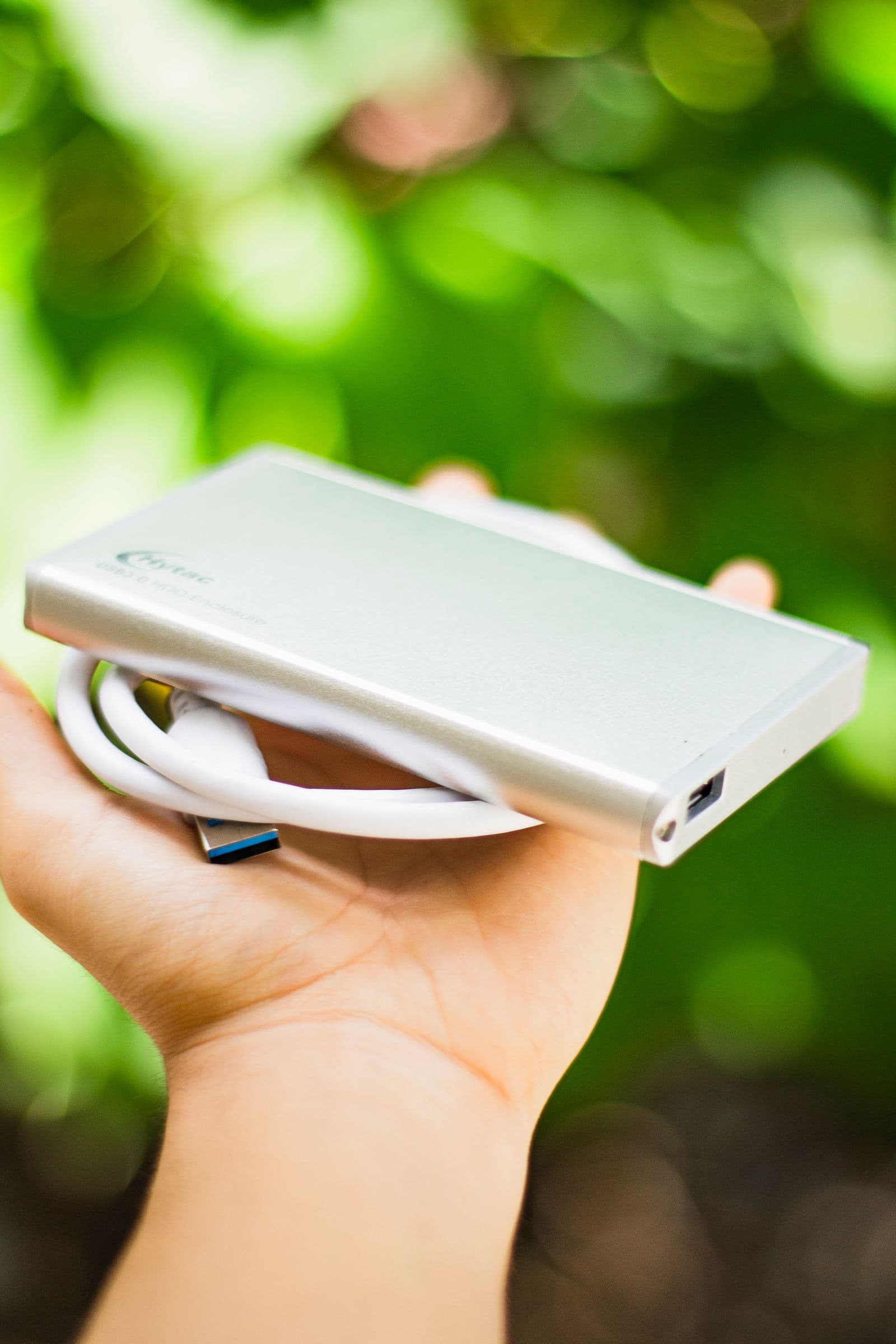 A hand holding a small external hard drive with its cable coiled around it